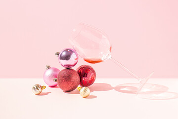 Trendy scene with wine glass, colorful Christmas bauble against pink background. Creative New year party concept.
