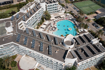 Aerial drone photo taken on the beautiful island of Majorca in Spain showing a top down view of a hotel building apartment with solar panels on the roof and and an out door swimming pool in the summer