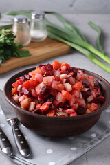Traditional Russian salad vinaigrette with beets, carrots, potatoes and onions in a clay bowl against a gray concrete background, Vegetarian food, Closeup
