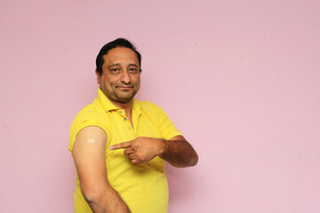 Latino mature adult man shows his arm recently vaccinated with band-aid against Covid-19 in the new...