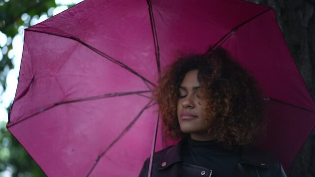 Woman holding pink umbrella outside daydreaming, Brazilian girl during rainy day