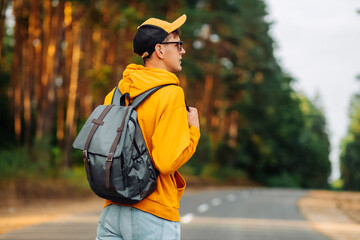 Happy male traveler with backpack traveling on the road along the forest trail. Camping