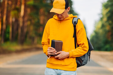 man praying outdoors while holding a Bible in his hands. A man in a yellow sweater and a cap holds...