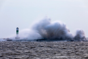 Fototapeta na wymiar The waves crashing on a pier with a lighthouse on lake Michigan
