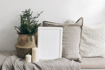 White blank wooden frame mockup. Christmas spruce tree, candles, linen cushions and plaid on the...