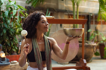 Hippy latina woman doing a performance with a tibetan bowl and stick at home