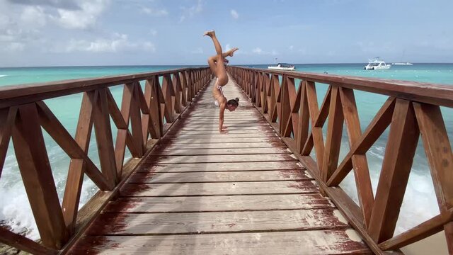 Flexible female circus doing handstand on the pier with sea and sky background. Travel, vacation and healthy lifestyle concept 