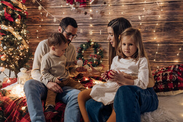 Family gives present to baby and daughter in living room decorated by christmas tree and xmas gift boxes. Portrait loving family holiday. Merry Christmas and Happy New Year. young parenthood
