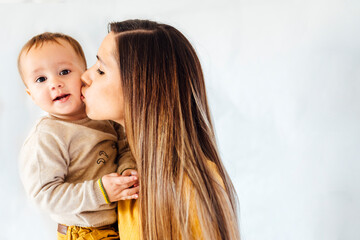 Portrait of young business mother kissing her baby boy in white background. Mum and son concept.