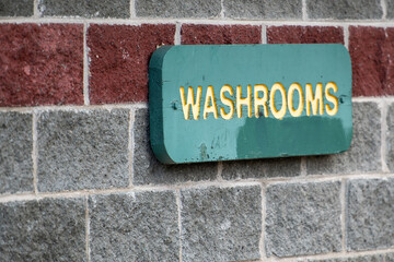 A washroom sign with yellow letters on a green wooden background. The sign is green in color. The...