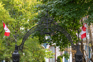 A vintage decorative black wrought iron fence with a large arched gate displaying two Canadian...