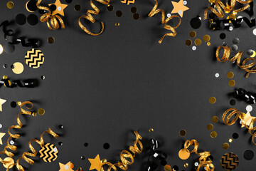 New Years party frame of shiny black and gold black and gold streamers and confetti. Top down view...