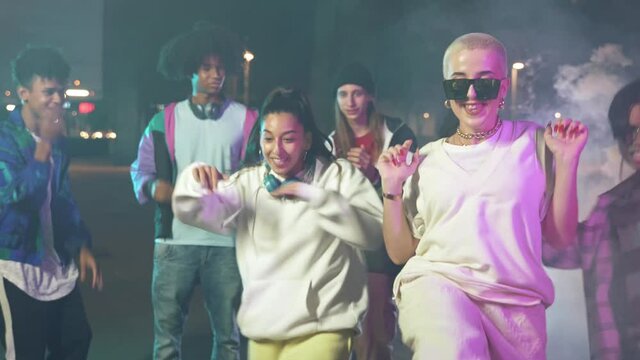Dancing young women and happy multi ethnic friends enjoying funky hip hop freestyle party dance together in city at night