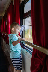 Pensive little boy looking through window traveling by train at comfortable railway carriage