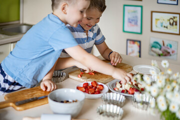 Happy little brothers preparing appetizing summer dessert with fresh fruits and berries together