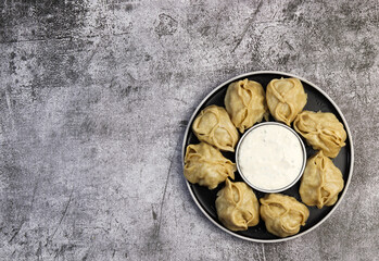 Manti - asian steam dumplings with sour cream sauce on a round plate on a dark grey background. Top view, flat lay