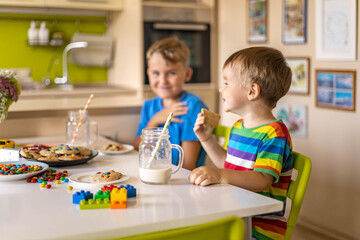 Funny male brothers eat cookies with round multi-colored sweets and drink milk.