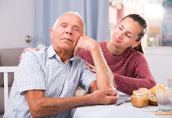 Portrait upset mature man sitting after conflict, daughter tries reconcile