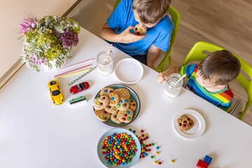 Funny male brothers eat cookies with round multi-colored sweets and drink milk.