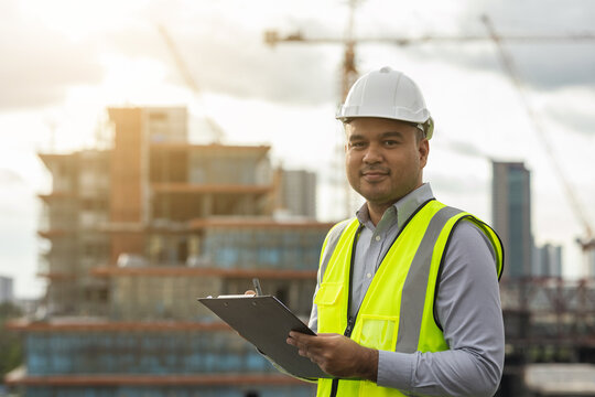 Inspector engineer man or architect with clipboard with white safety helmet in city construction site. Checking with checklist on rooftop building construction at capital.