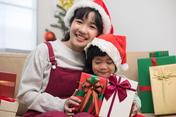 Obraz na płótnie Canvas Cute Asian family Mother and son giving the present gift box each other. In the christmas eve festival. Mom and little child dressing christmas theme sitting on sofa with happy moment new year's day