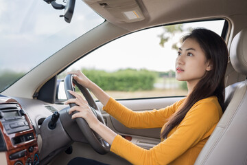 Naklejka premium Young beautiful asian women getting new car. she very happy and excited Look the rearview mirror while reversing the car. Smiling female driving vehicle on the road on a bright day