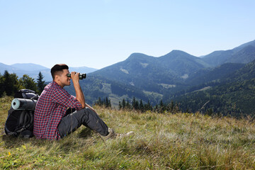 Tourist with hiking equipment looking through binoculars in mountains