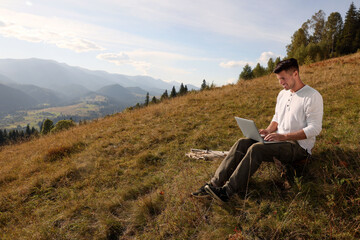 Naklejka na ściany i meble Man working with laptop outdoors surrounded by beautiful nature. Space for text