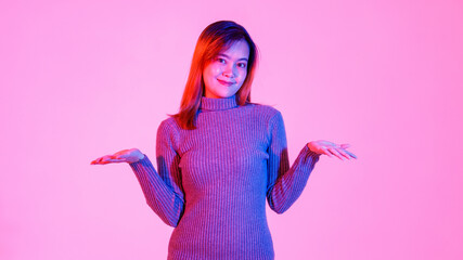 Portrait studio shot of millennial Asian young teen female model in gray turtleneck sweater standing holding empty hands up presenting advertising choosing product option on pink light background