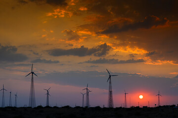 Silhouette of wind mills in twilight with a setting sun and cloudy sky in background, Rajasthan,...