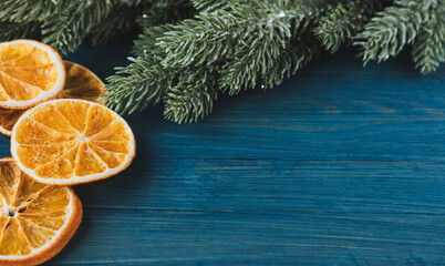 Fototapeta na wymiar New Year's composition of dried orange slices and artificial spruce branches on a blue wooden background with a place for text