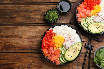 Delicious poke bowls with salmon and vegetables served on wooden table, flat lay. Space for text