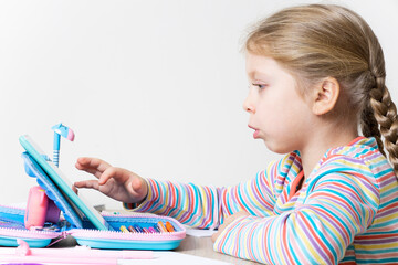 The girl is engaged in online education on the tablet at the table in the children's room. Child...