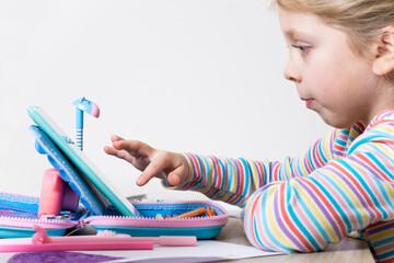 Online education for children. The girl is reading an e-book. The child draws in online courses....