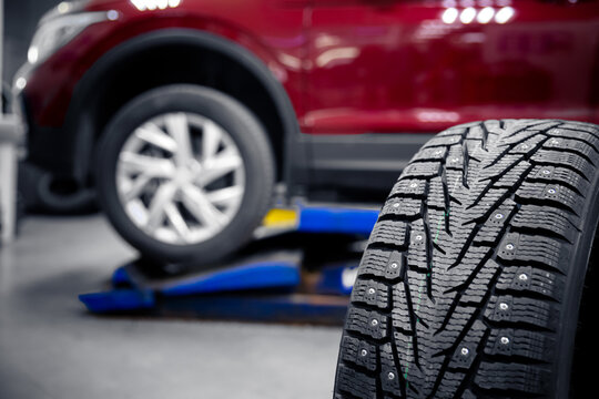 Selective focus winter tire with steel studs in service, in background car is lifted on lift