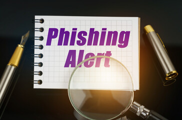 On the black surface is a pen, a magnifying glass and a notebook with the inscription - Phishing...