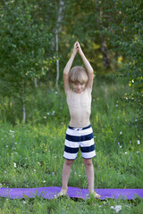 Boy practising yoga outdoor in green park, performs variant of mountain pose, with his hands raised, called asana Talasana