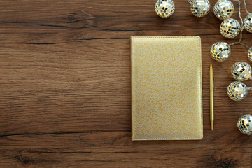 Golden planner, pen and Christmas lights on wooden table, flat lay. Space for text