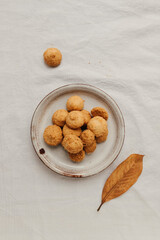 Round small cookies on a light plate on a white cotton tablecloth, top view