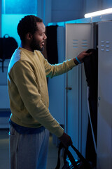 Young sportsman with bag taking jacket or hoodie out of locker before changing clothes for sports training