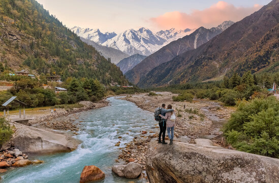 Tourist couple enjoy a vacation at the scenic Baspa river valley with view of Himalaya mountain range at Rakchham, Himachal Pradesh, India