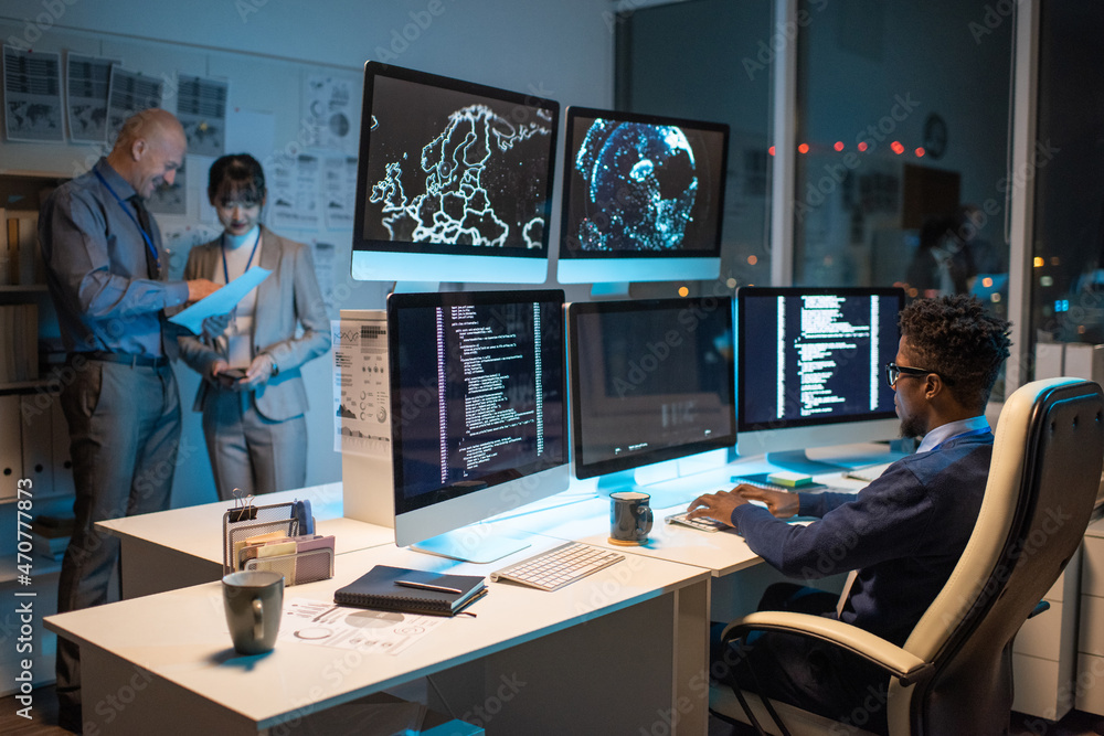 Poster young african businessman looking at data on computer screen while sitting in armchair in front of s
