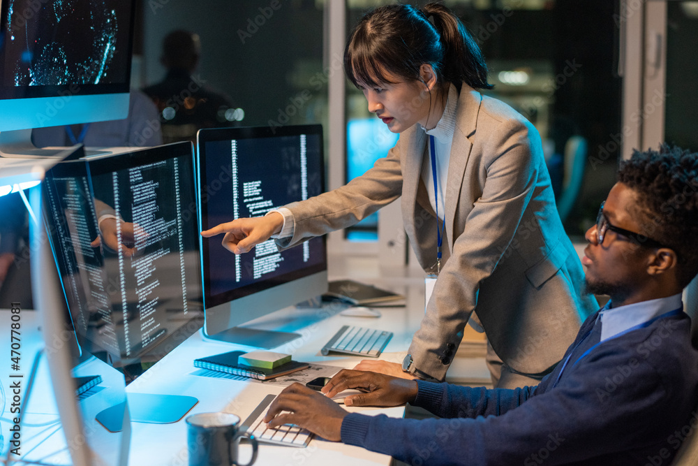 Aufkleber Young Asian female it-engineer pointing at data on computer screen while discussing working point with African male colleague