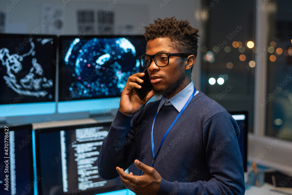 Poster Young serious software developer or it-engineer consulting client on mobile phone while standing against his workplace