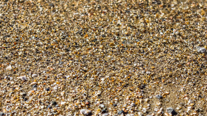 A background of sand, small pebbles and flowing waves on the sea beach. Summer vacation and coastal nature concept