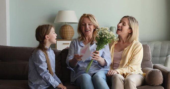 Older mother grandma feel grateful receiving tender bunch of daisies birthday card made with love from adult daughter grandkid girl. Smiling mum child greet senior granny give flowers gift on March 8