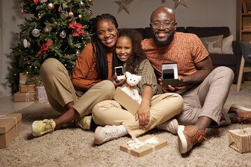 Cheerful family members with open giftboxes showing their xmas presents while sitting on the floor...