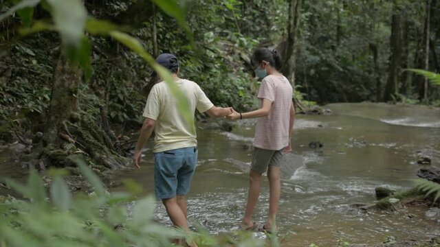 Asian mother and her teenager daughter wears face mask walking over the creek together in the tropical forest. Family nature travel activities. Phang Nga Province. Thailand.