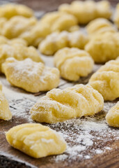 Vertical view uncooked potato gnocchi with flour and grated parmesan cheese over wooden cutting board. Macro, selective focus. Home cooking