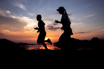 Silhouette of a couple running at sunset with the sun in the background near flood dams and...
